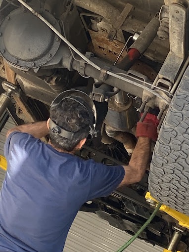 Mechanic in welding helmet repairs undercarriage of raised vehicle, using tools. Auto repair, automotive maintenance.