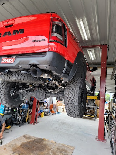 Red Ram 4x4 truck raised on a lift, rear view showing exhaust and undercarriage. Auto repair shop setting.