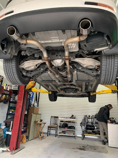 Car's undercarriage, raised on a lift in an auto repair shop, reveals the exhaust system and components during maintenance or repair.