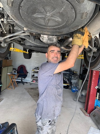 Mechanic working under a raised vehicle, wearing gloves and a grey shirt. Auto repair, car maintenance.