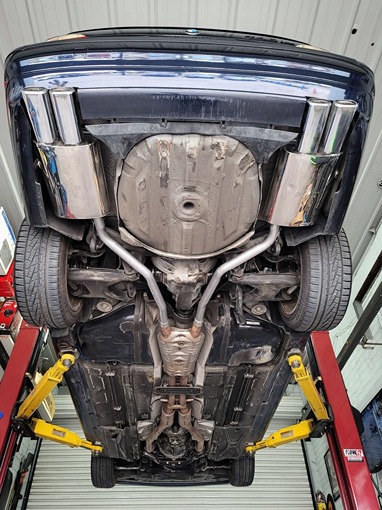 Undercarriage view of a car raised on a lift, showcasing a detailed view of its exhaust system, including dual exhaust pipes and catalytic converter.